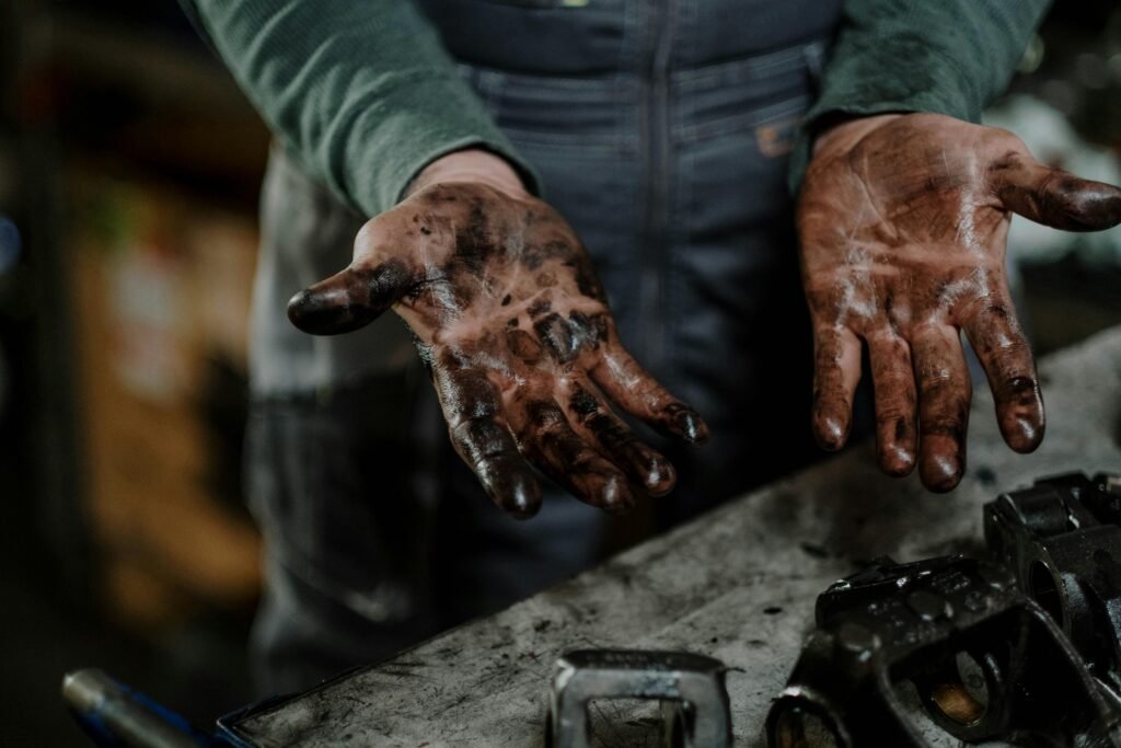 Close-up of a mechanic's dirty hands in a garage workspace with grease and spare parts.